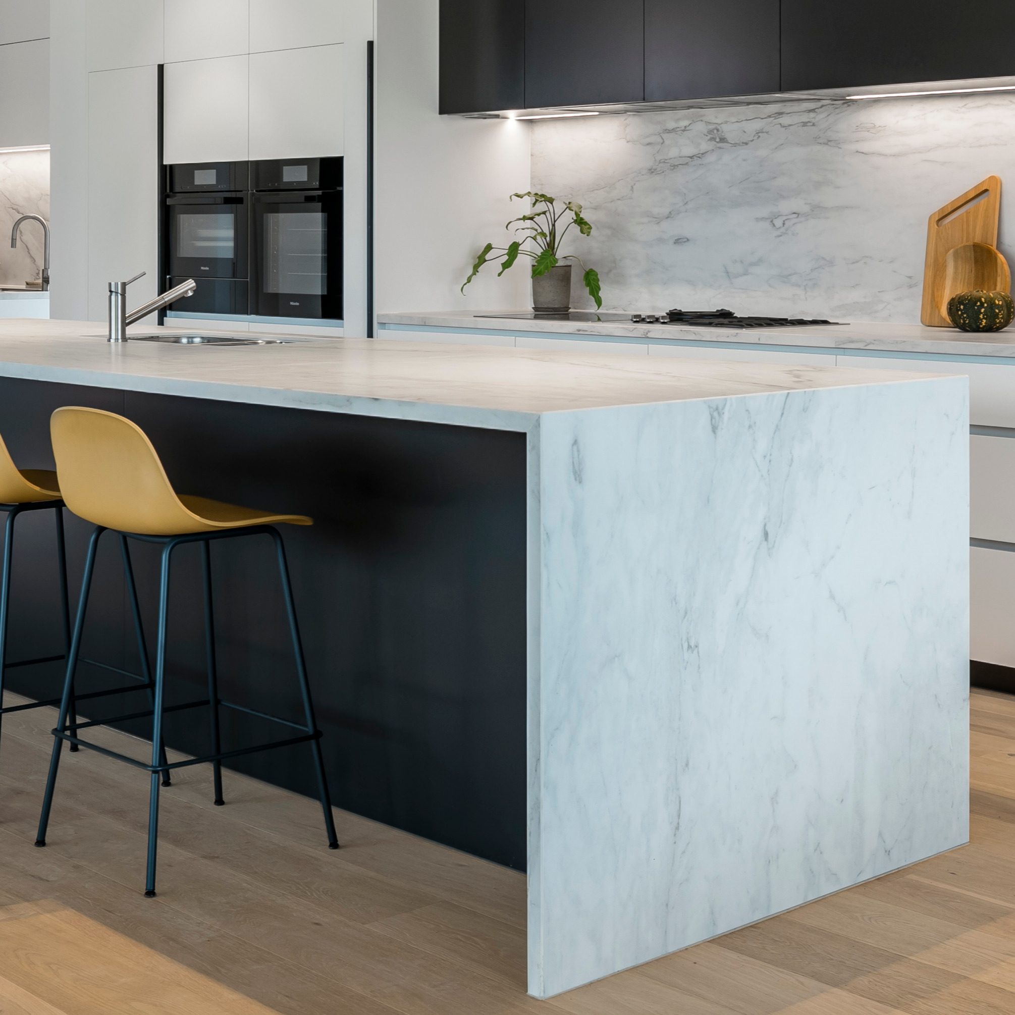 Modern kitchen interior featuring a sleek Dekton stone benchtop with a marble-like finish, complemented by black cabinets and wooden bar stools.